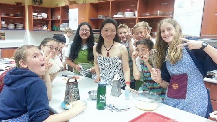 Ying and the students in her cooking class pull silly faces after learning to make dumplings during a school visit. 
